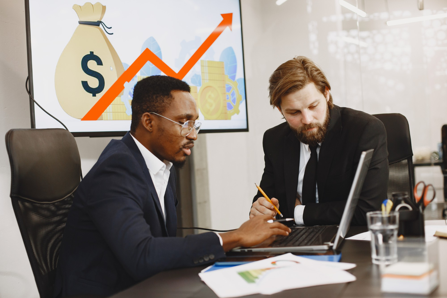 Two business analysts checking business trends report, in an office environment with charts and graphs on the whiteboard in the background.