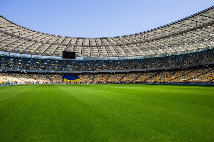 A large field of stadium with empty seats and wide angle photo showing the clear blue sky.