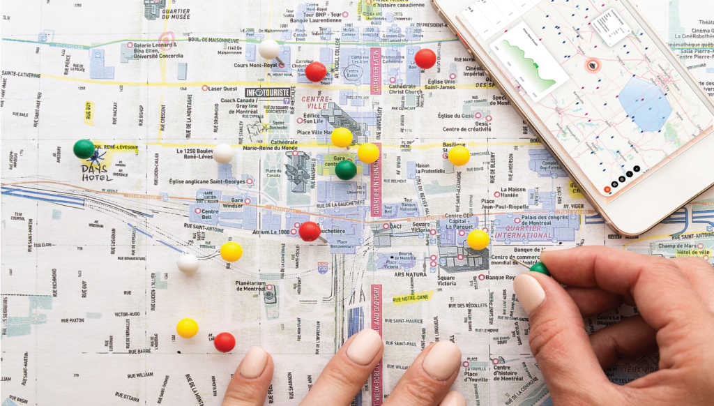 Paper map spread over table, a person is placing the pins to mark the locations.